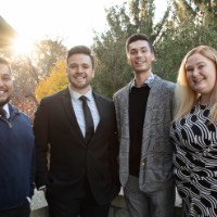 Group of four people pose outside with sun setting behind them